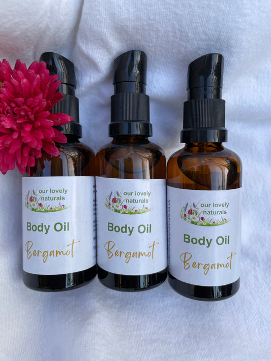 Three bottles of 'Our Lovely Naturals' Body Oil - Bergamot Body Oil with a pink flower on a white background.