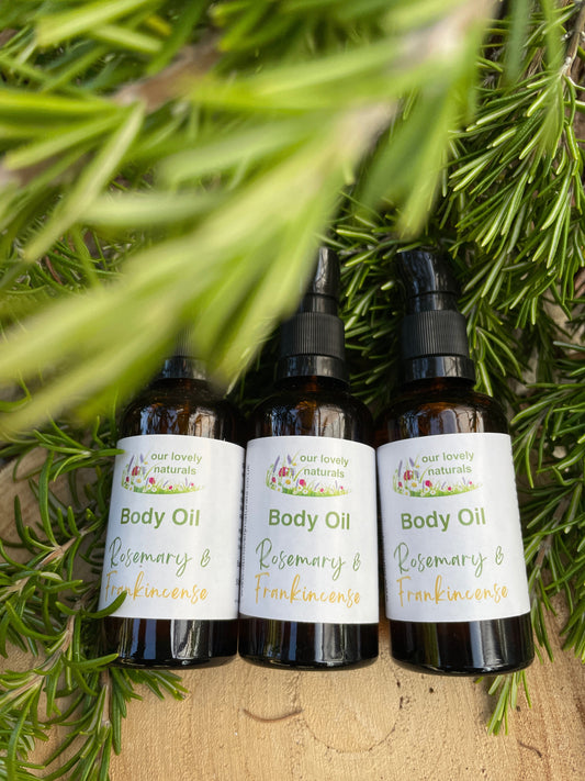Three bottles of Body Oil - Rosemary & Frankincense with labels on a wooden surface and green leaves in the background