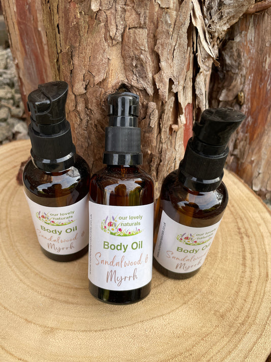 Three bottles of 'Our Lovely Naturals' body oil - Sandalwood & Myrrh with labels on a wooden surface.