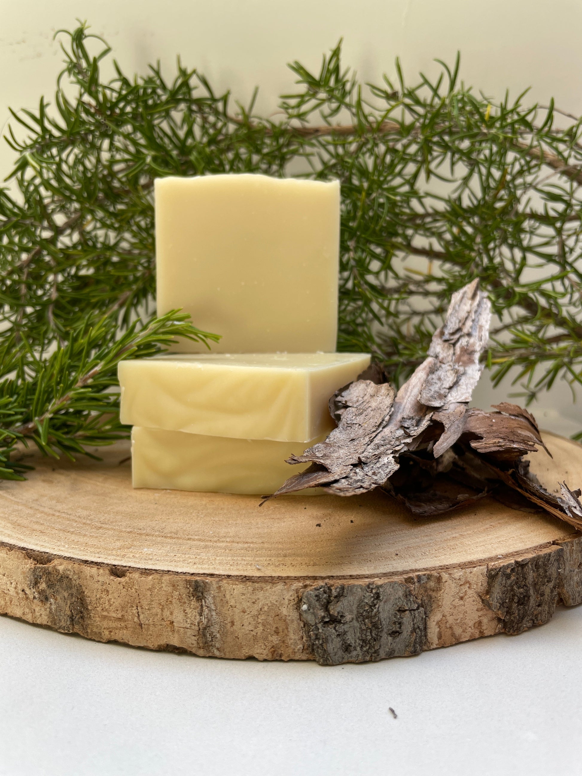 Three bars of soap on a wooden surface with greenery in the background